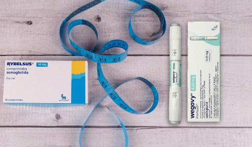 Rybelsus 14mg tablets box vs Wegovy 0.25mg injection pen with a blue measuring tape on a wooden background for weight loss comparison.
